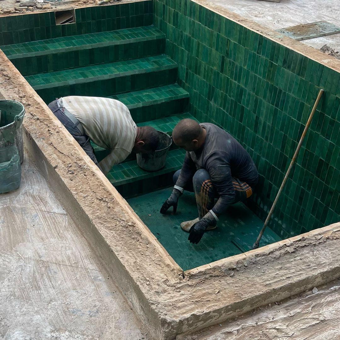 Artisans posant du zellige vert dans une piscine